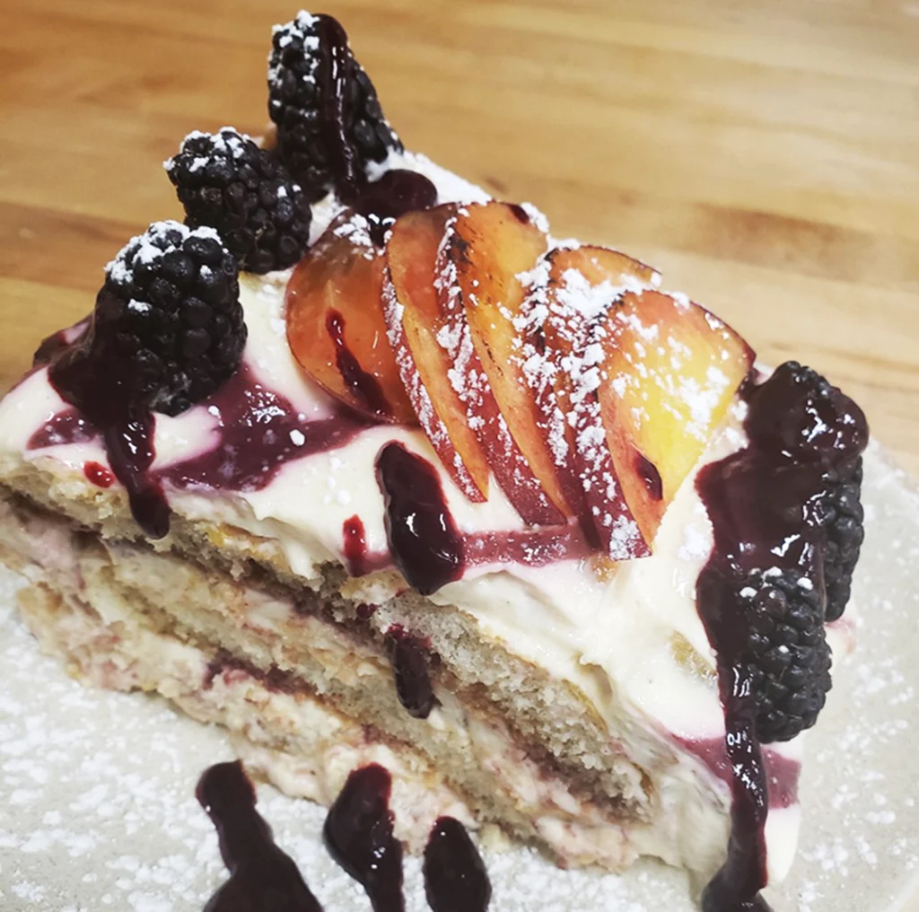 Peaches and blackberries on top of tiramisu on plate.